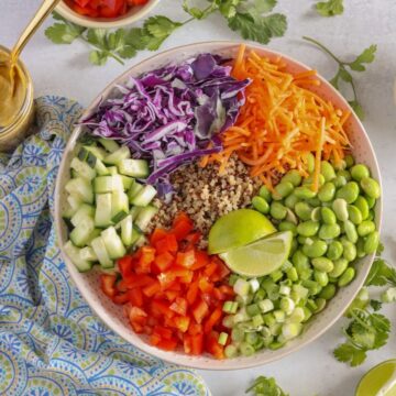 colorful salad bowl on white counter with peanut sauce and colorful napkin