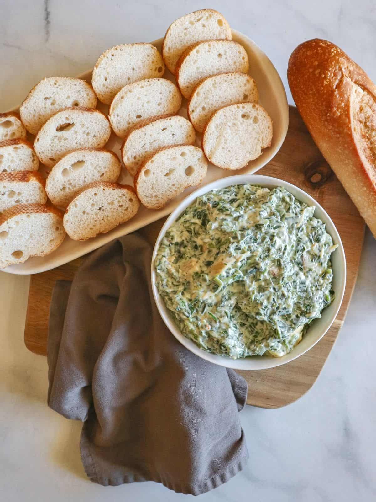 Cutting board with bowl and plate full of sliced bread and grey napkin. 